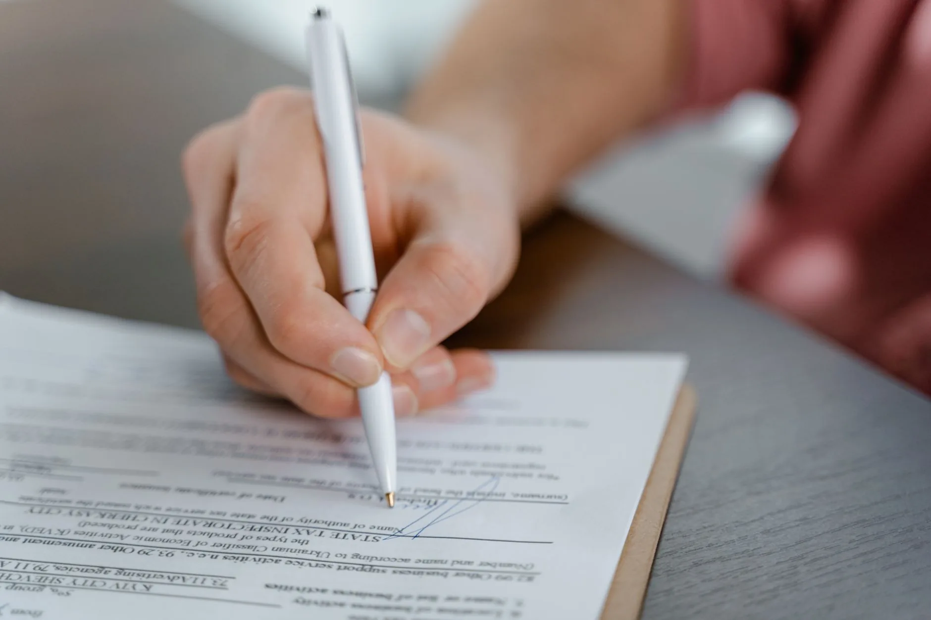 Gwo plan yon moun k ap siyen yon dokiman ofisyèl ak yon plim